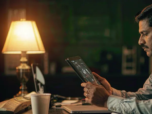playrupees Man studying match data on a tablet beside a cricket bat and coffee