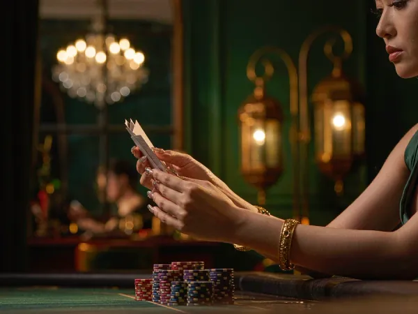 playrupees Hands with gold bangles holding three cards above green felt beside chips