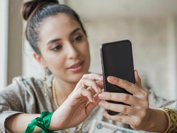playrupees Hands holding a phone with an abstract payment screen above a wooden table